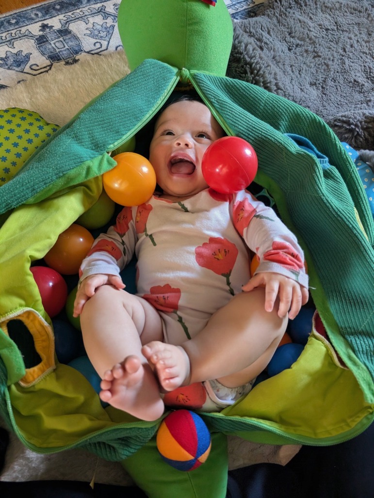 Jojo leaning back in a ball pit kicking her legs playfully